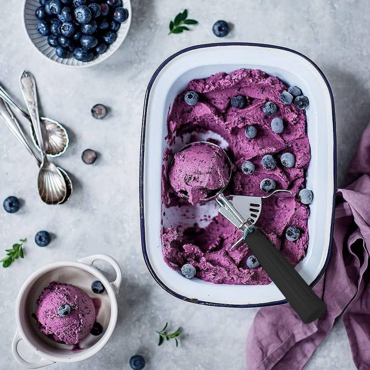 Black trigger ice cream scoop with stainless steel bowl in a tub of blueberry ice cream