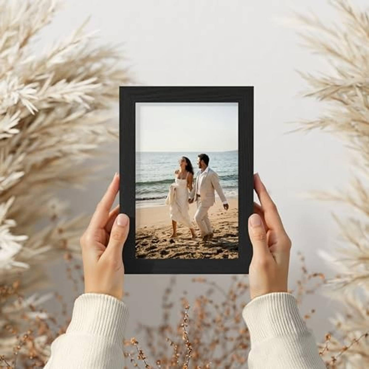 Black picture frame held in hands, showing a beach photo inside a white mat