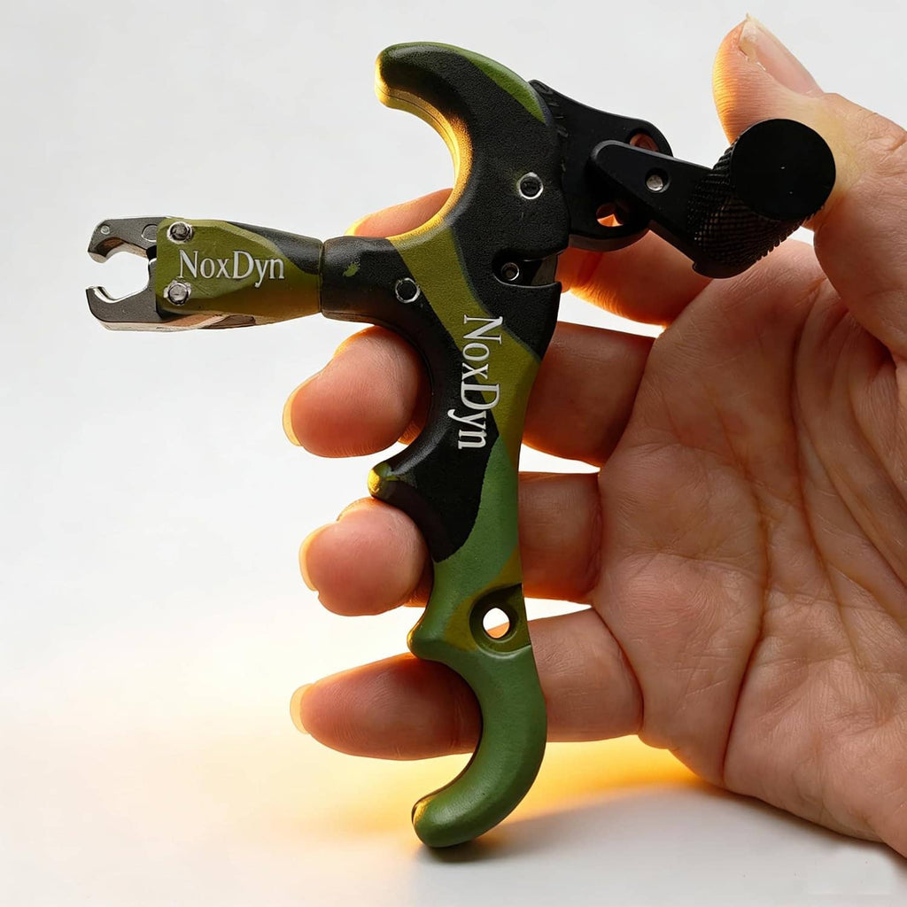 Thumb archery release held by hand, camo green/black body, textured trigger knob, NoxDyn