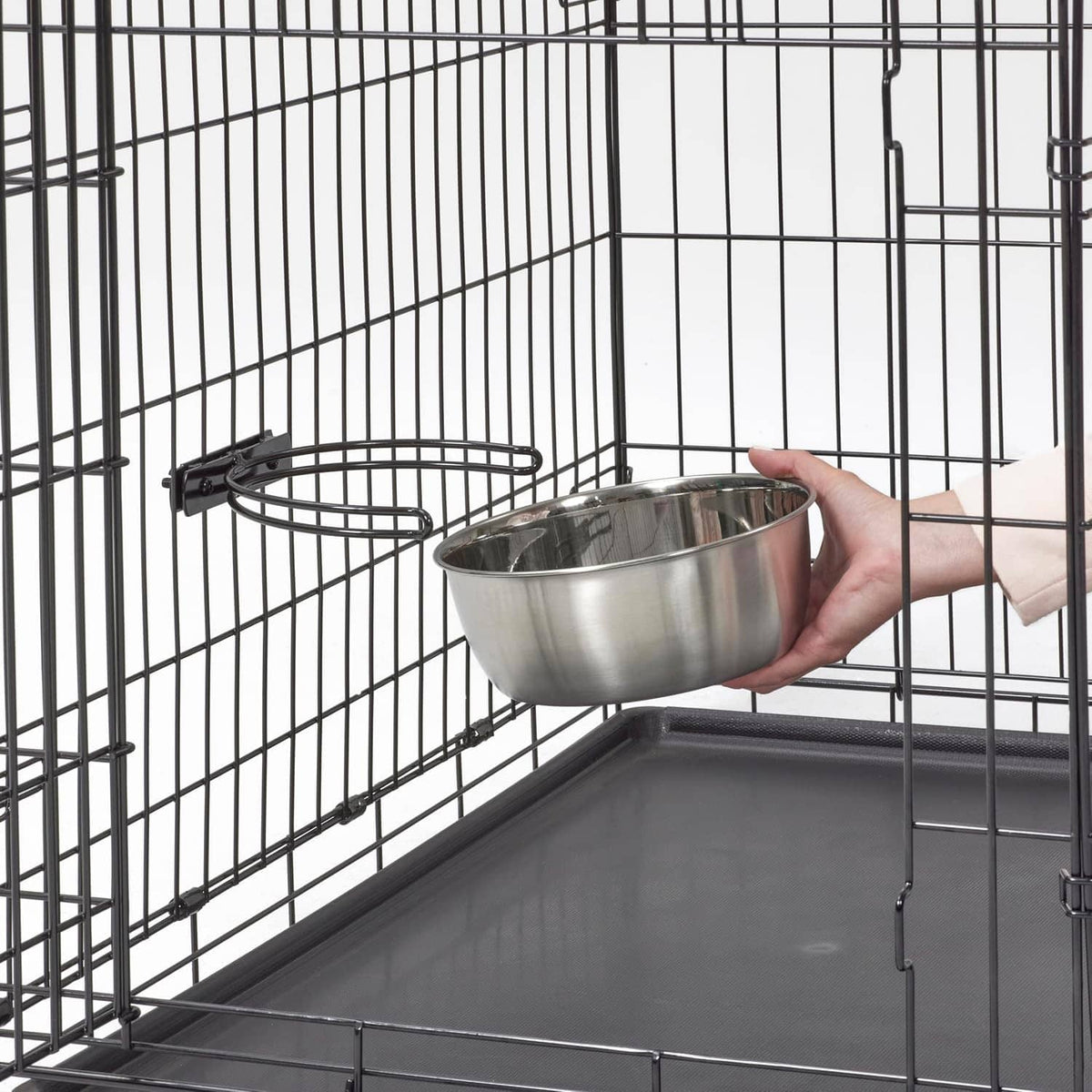 Hand holding a stainless steel bowl inside a black wire dog crate
