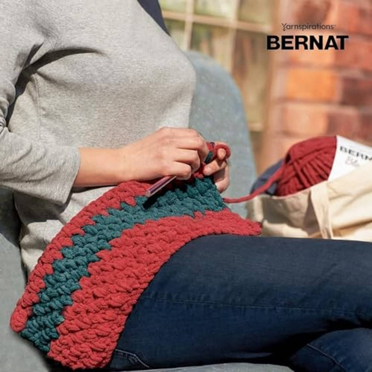 Two-tone chunky crochet blanket in red and teal, laid across a person’s lap