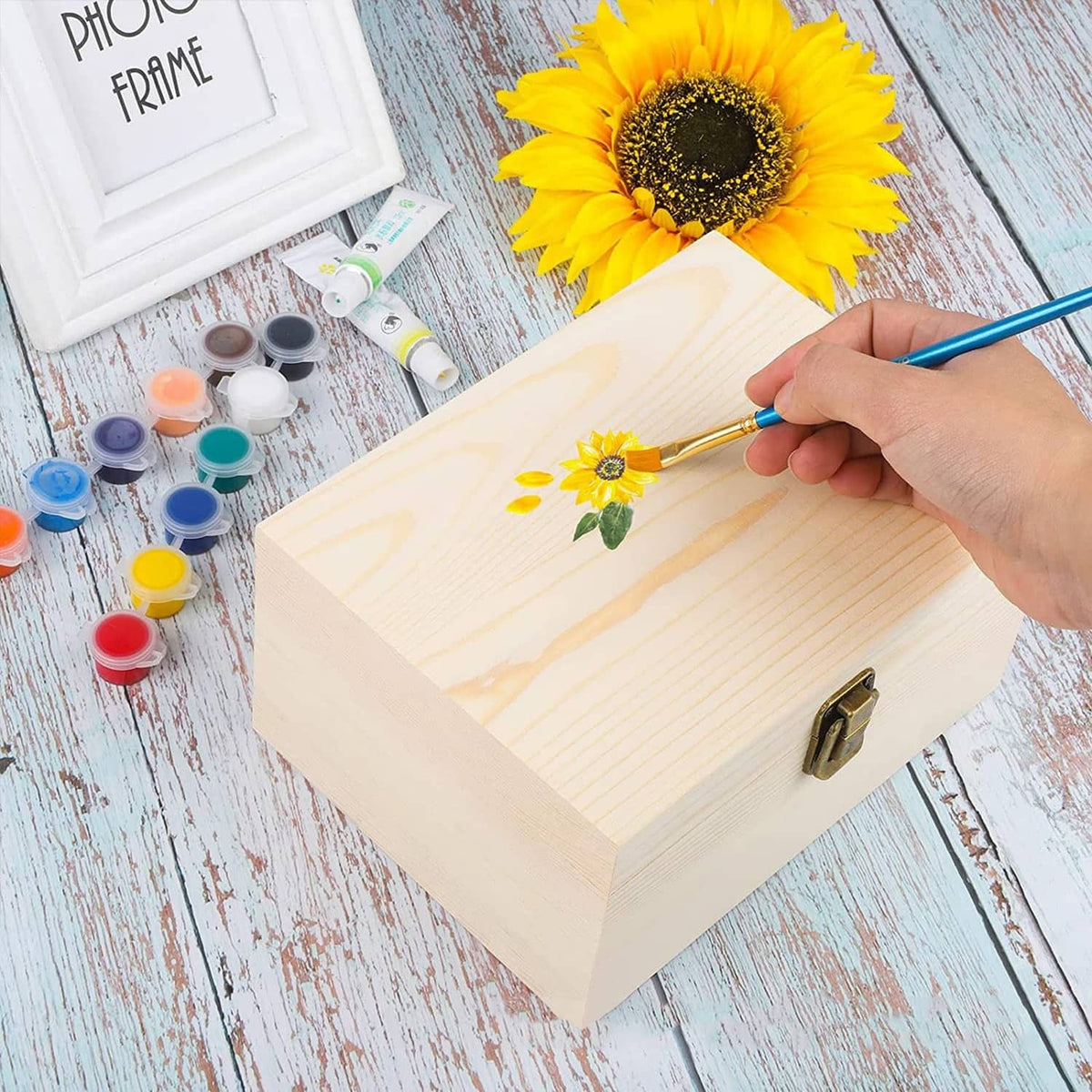 Unfinished wooden box with hinged lid and metal clasp, being painted with flower artwork.