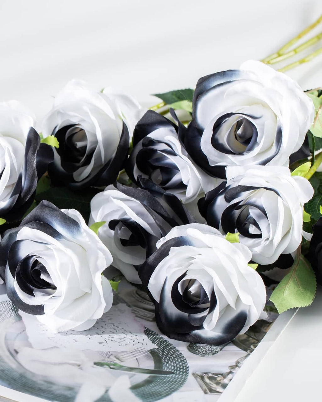 Artificial rose bunch with white and black blooms and green leaves, laid on mesh