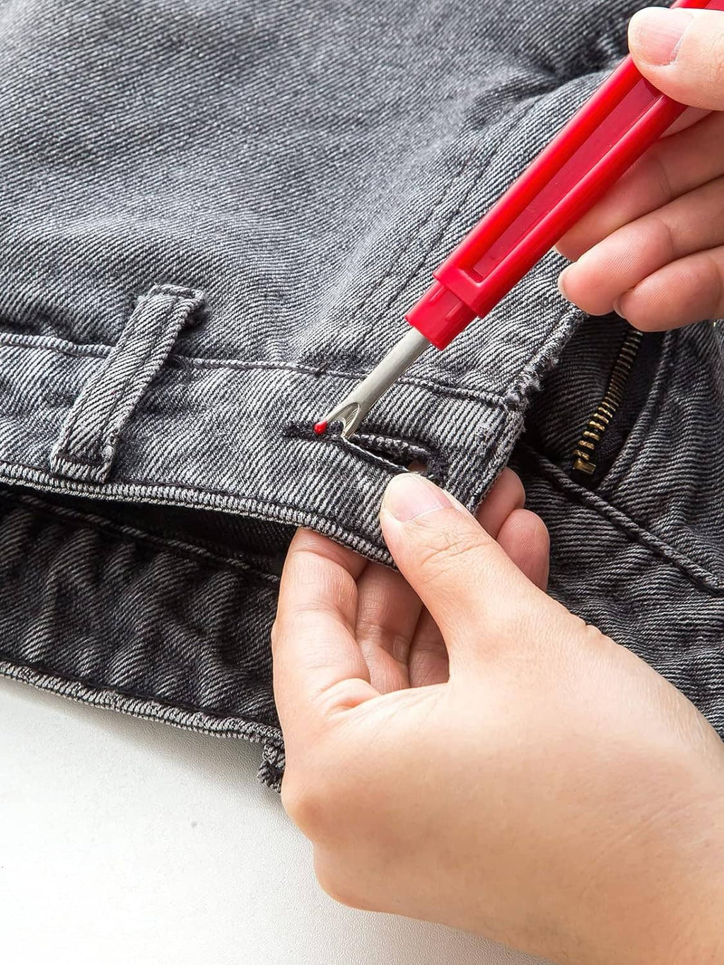 Red seam ripper tool lifting thread on dark denim jeans seam
