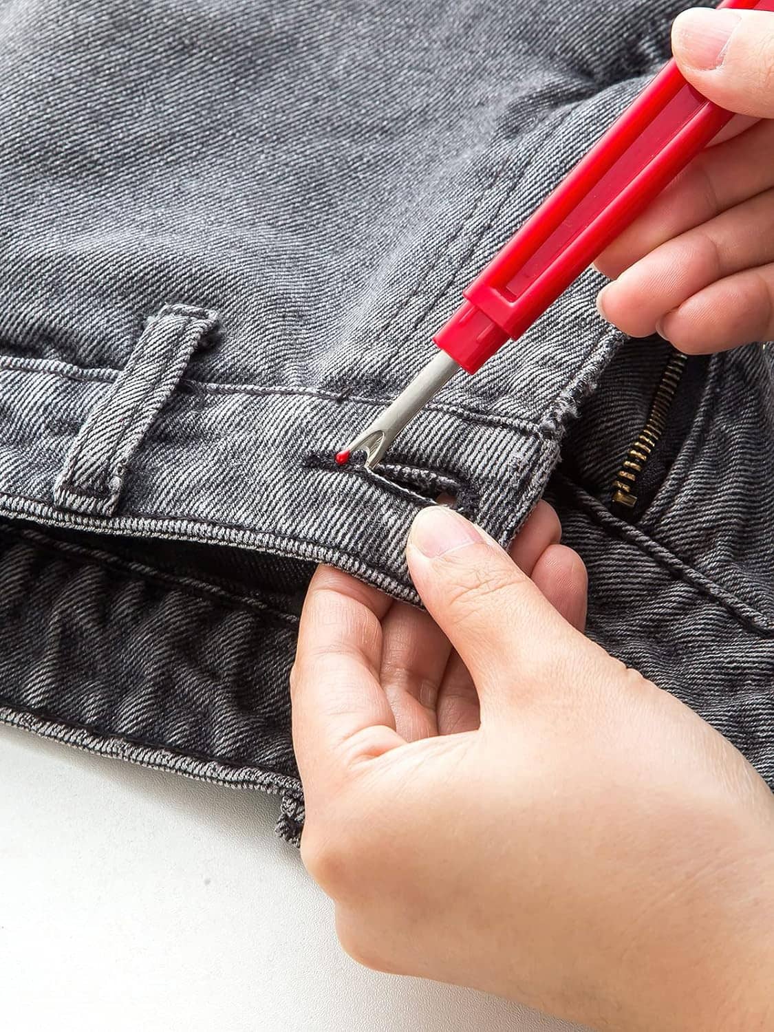 Red seam ripper tool lifting thread on dark denim jeans seam