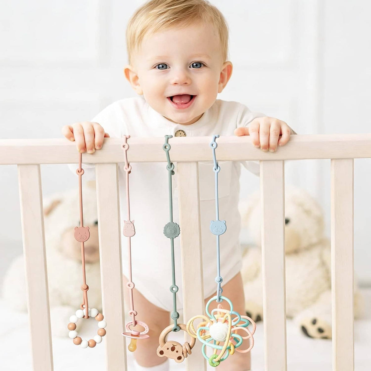 Baby holding a wooden bar with hanging silicone toy straps and multiple teether charms