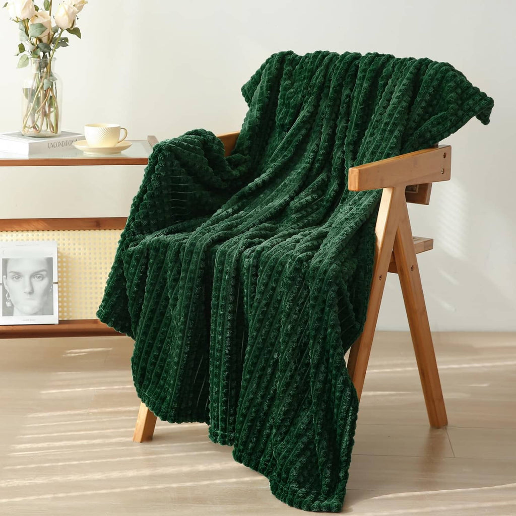Dark green flannel fleece throw blanket with raised waffle texture, draped on wooden chair