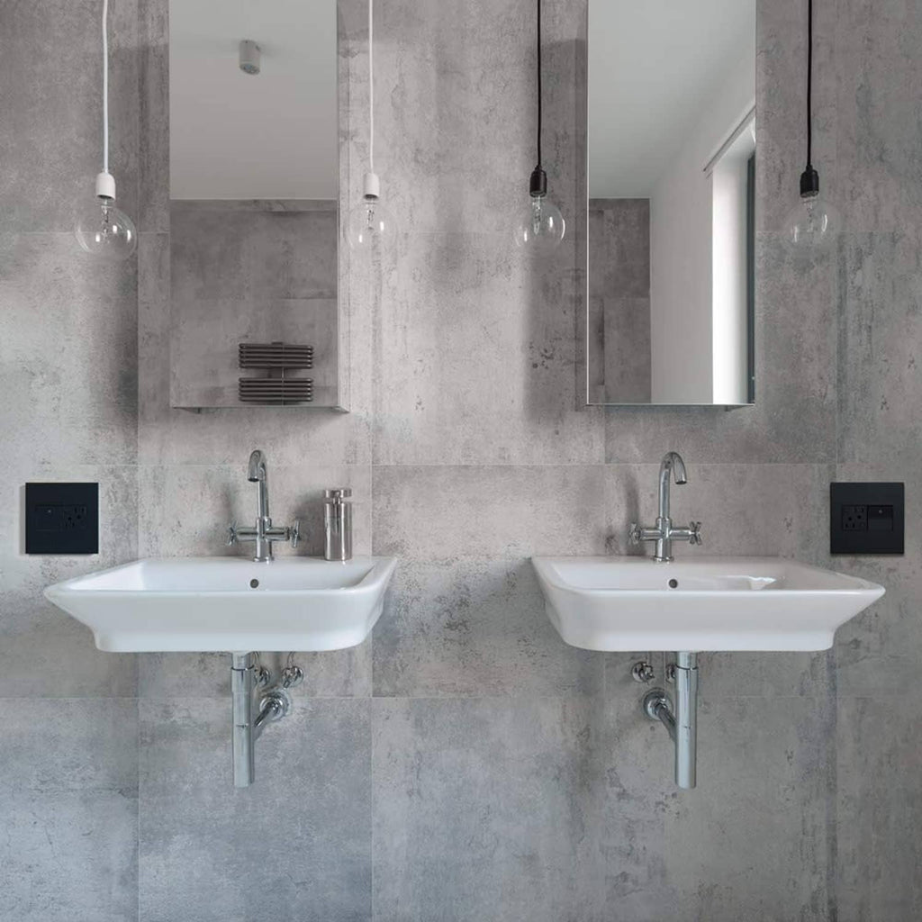 Two graphite 2-gang wall plates with outlets on a light gray tile wall