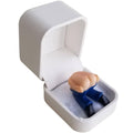 White ring gift box with open lid and blue prank ring on gray insert