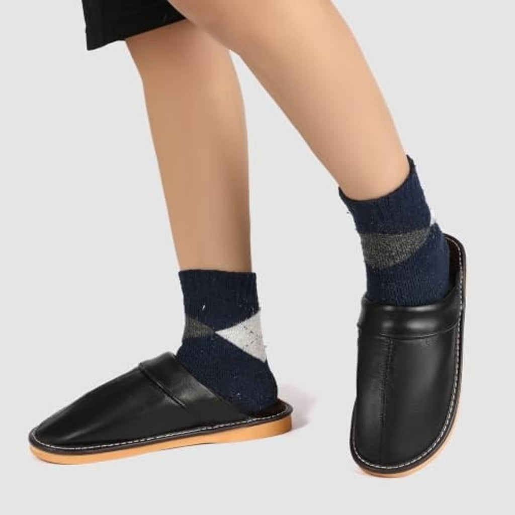 Black leather slip-on slippers on feet with navy socks and tan sole