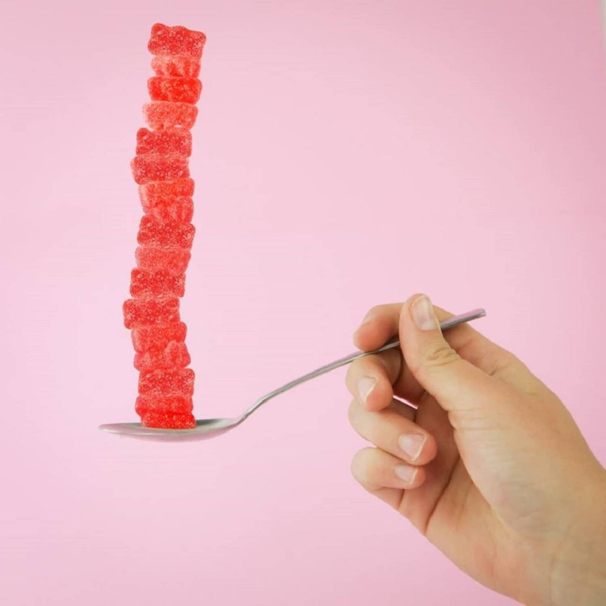 Hand holding a spoon with a line of red sour gummy bears