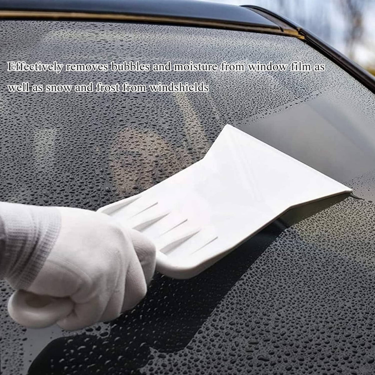 Long-handled squeegee scraper removing bubbles from window film on glass