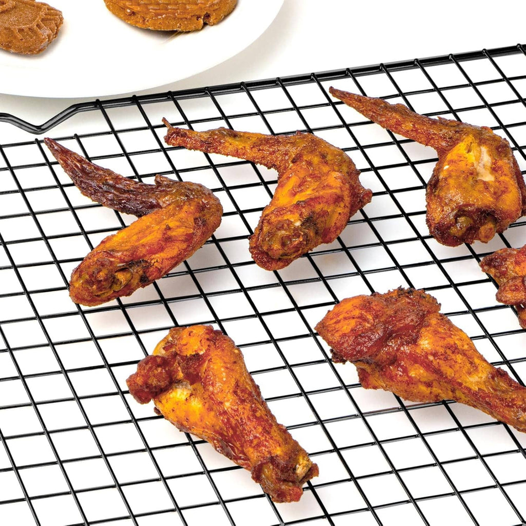 Black wire cooling rack with baked chicken pieces cooling on the grid.