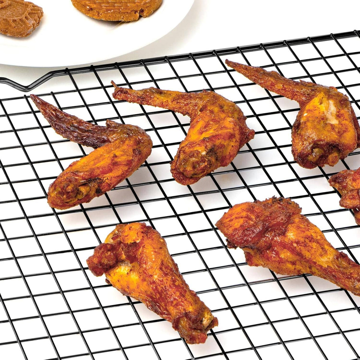 Black wire cooling rack with baked chicken pieces cooling on the grid.