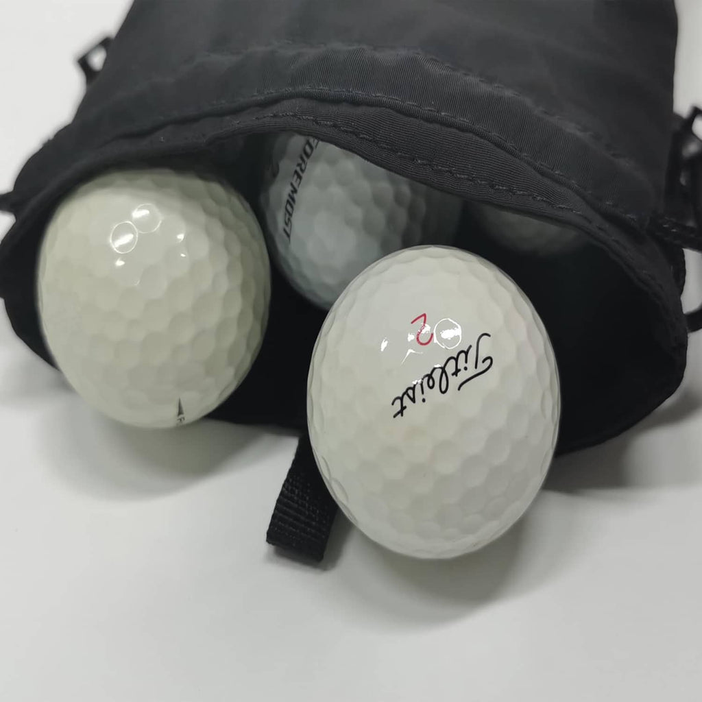 Black drawstring pouch holding three golf balls, with white print on the balls.