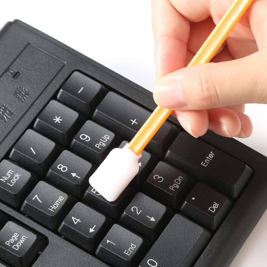 Orange foam swab cleaning between keys on a black keyboard.