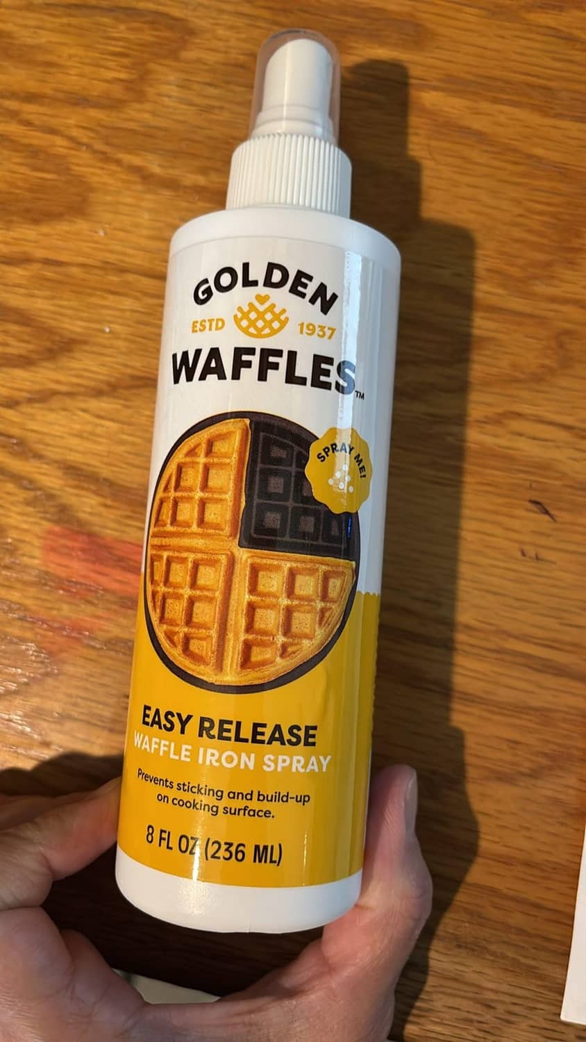 Waffle iron spray bottle held in hand, white with amber yellow label and pump sprayer