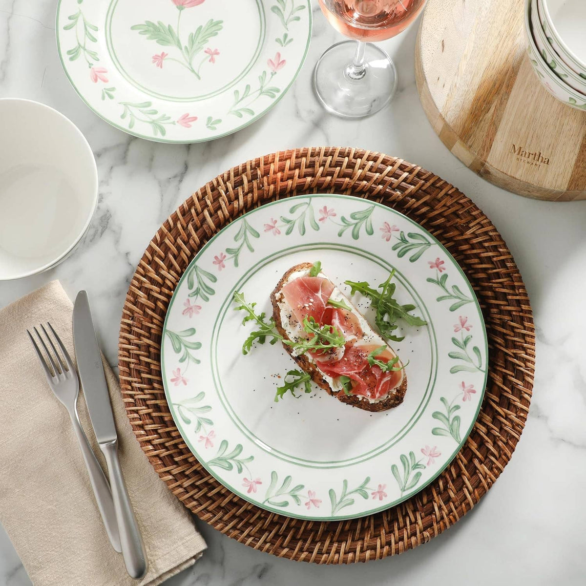 Floral dinner plate with green border and pink flowers, topped with cured meat and greens