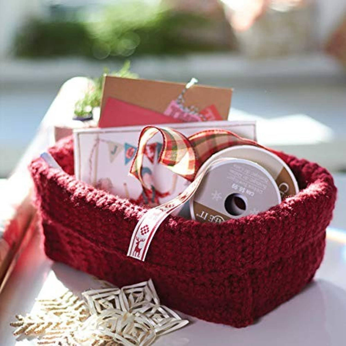 Chunky knit burgundy yarn basket holding small wrapped gifts and a spool-like item