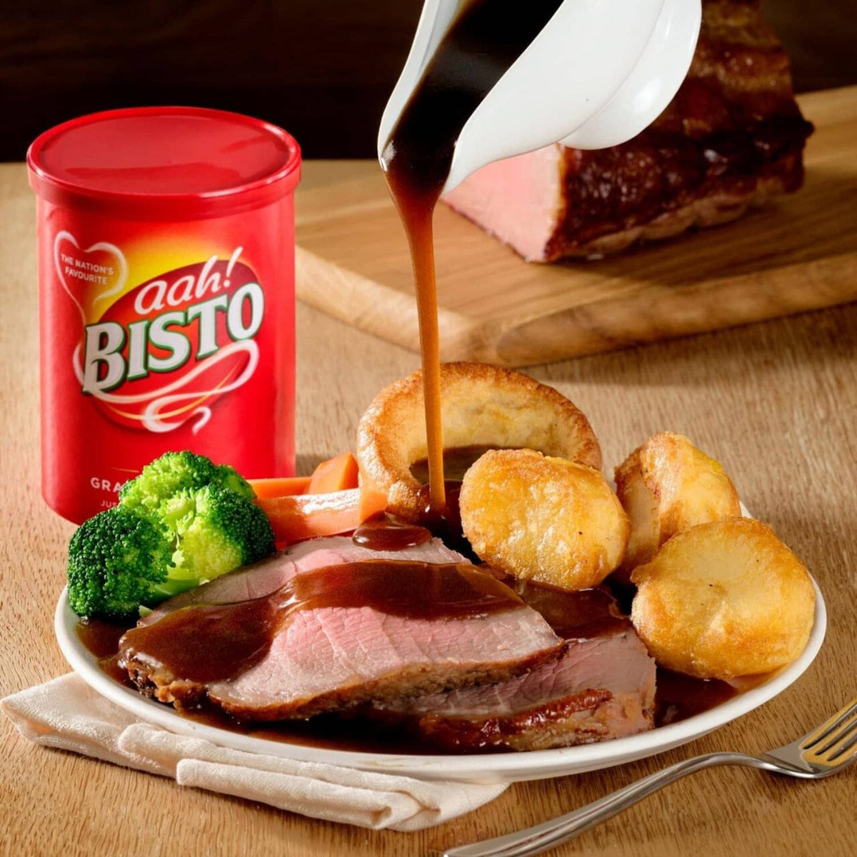 Bisto instant gravy granules tub with pour of brown gravy over roast dinner plate