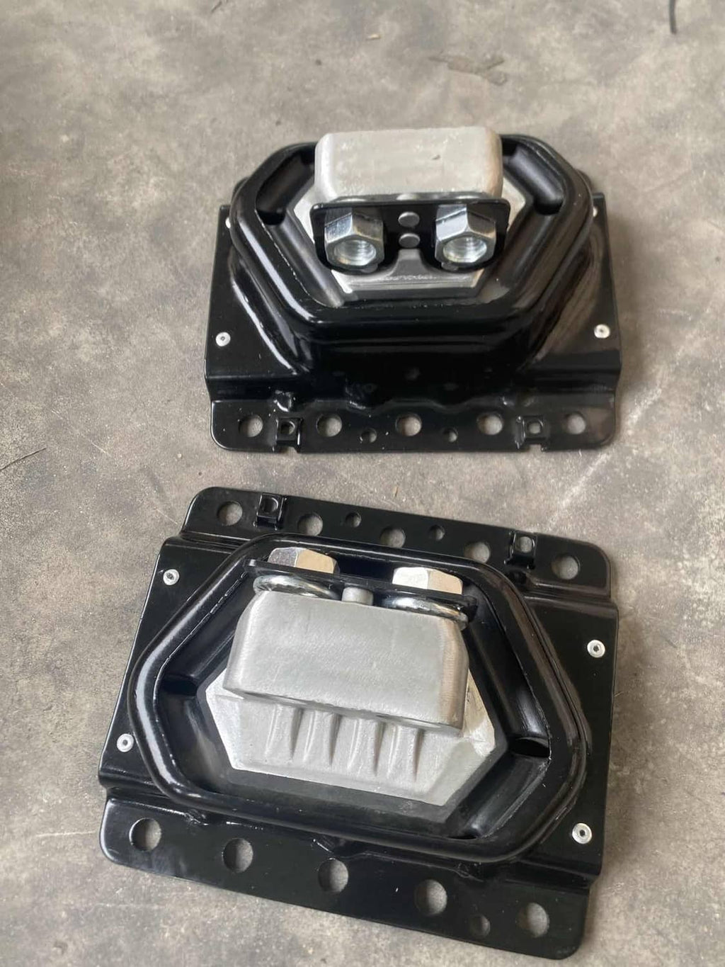 Two black engine mounts with silver bushings, photographed on a flat surface