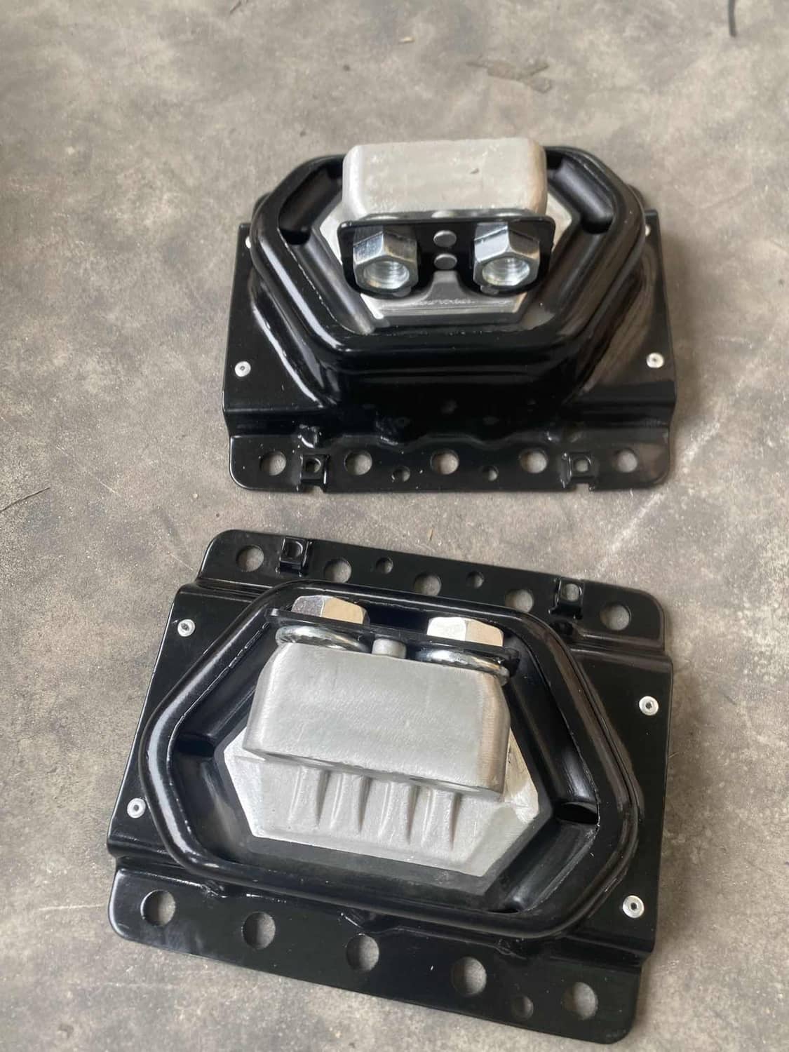 Two black engine mounts with silver bushings, photographed on a flat surface