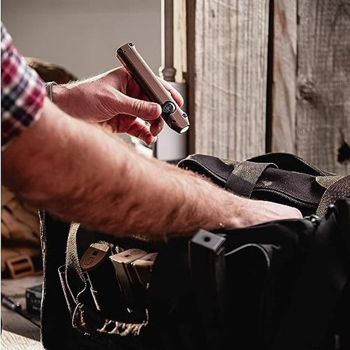 Handheld coyote tan flashlight clipped to a strap while carried in a pouch