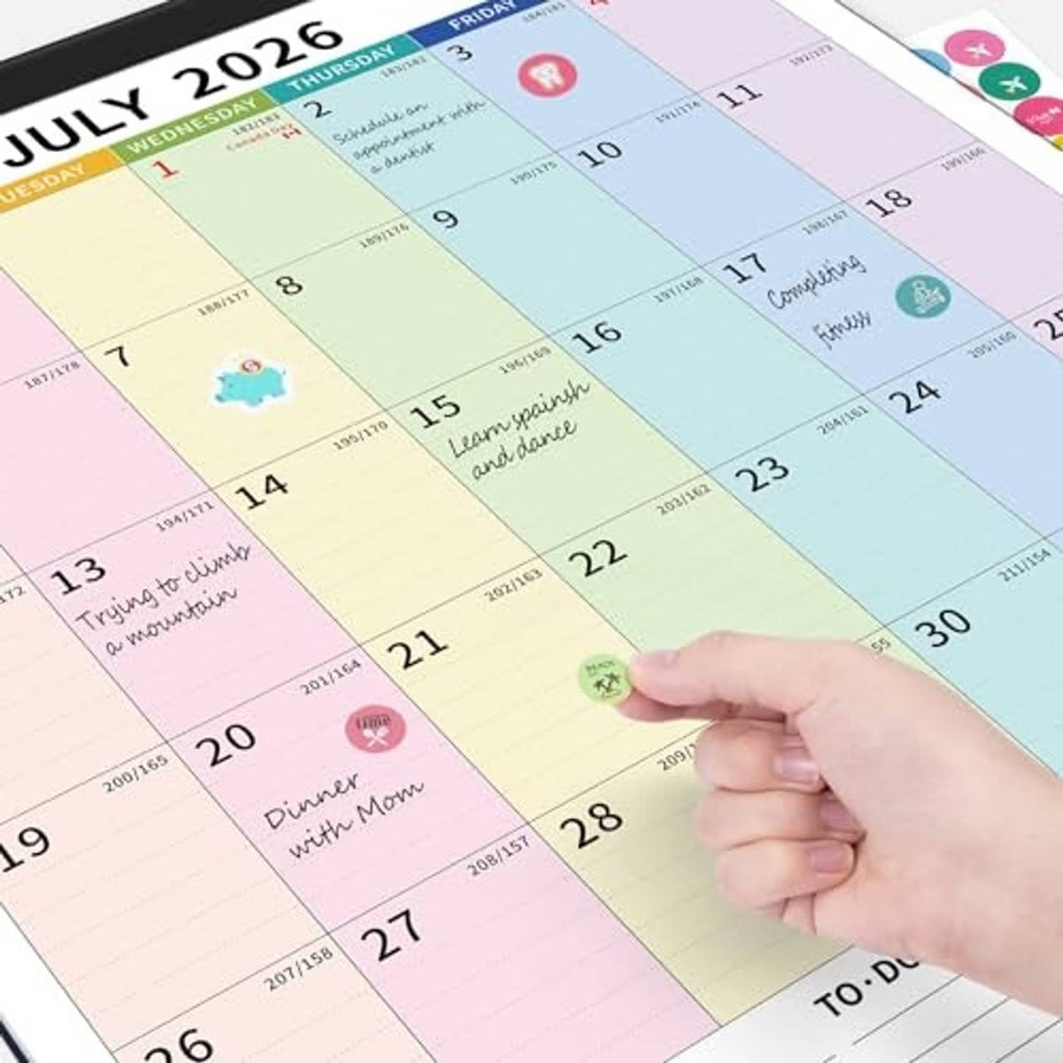 Hand marking a July 2026 monthly calendar, colorful date grid with to-do area