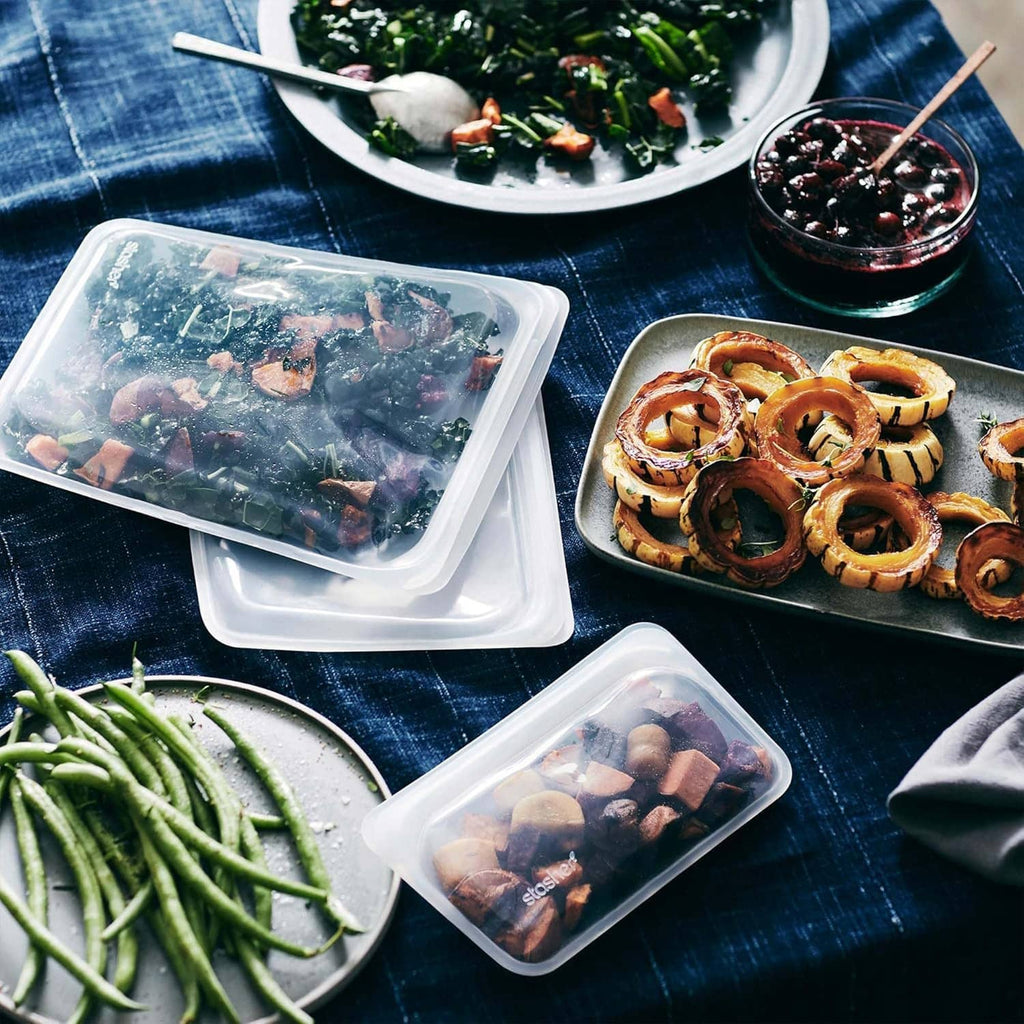 Reusable silicone food storage bag with clear lid, holding cooked food and greens