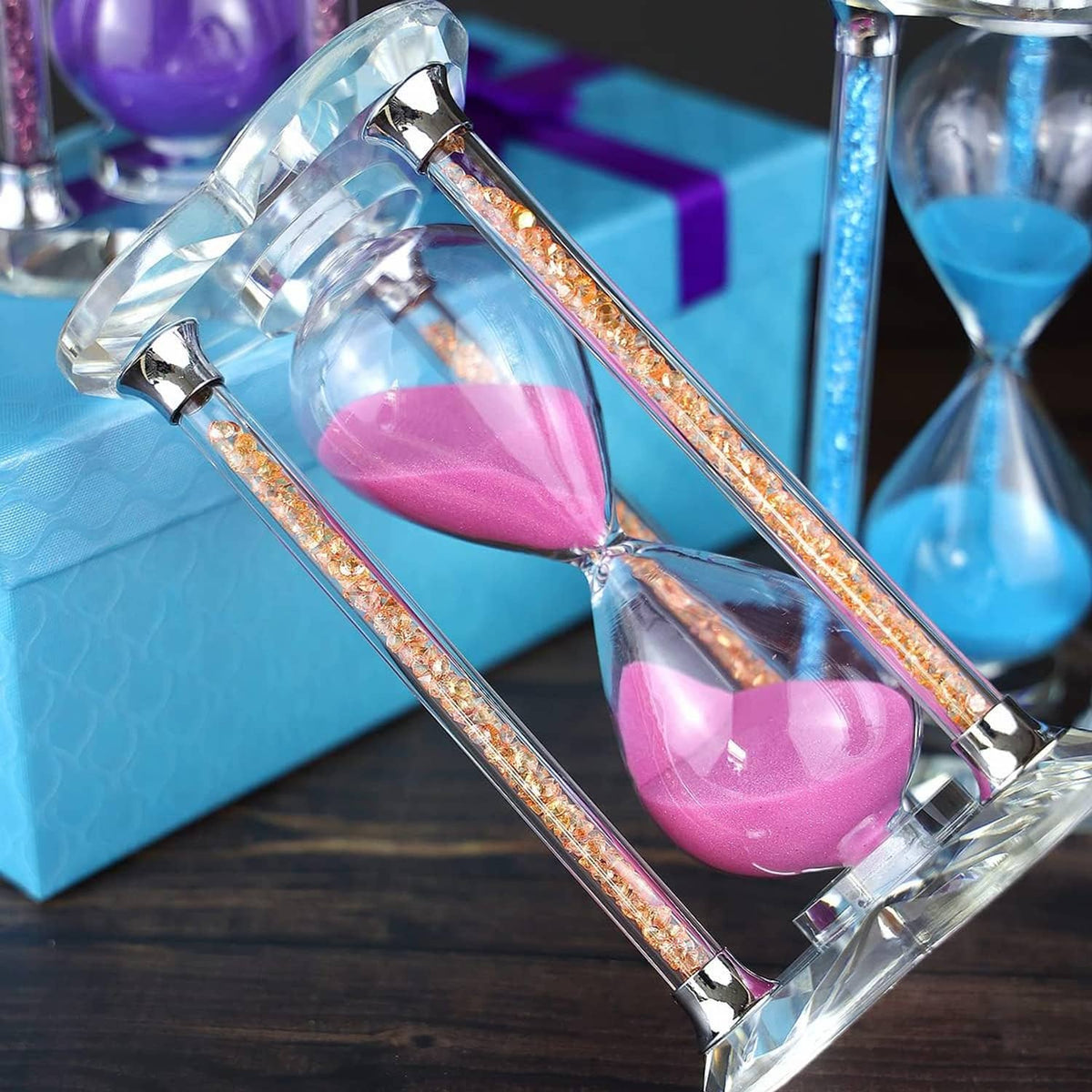 Tilted view of heart-shaped pink sand hourglass with clear glass and glittering gold trim