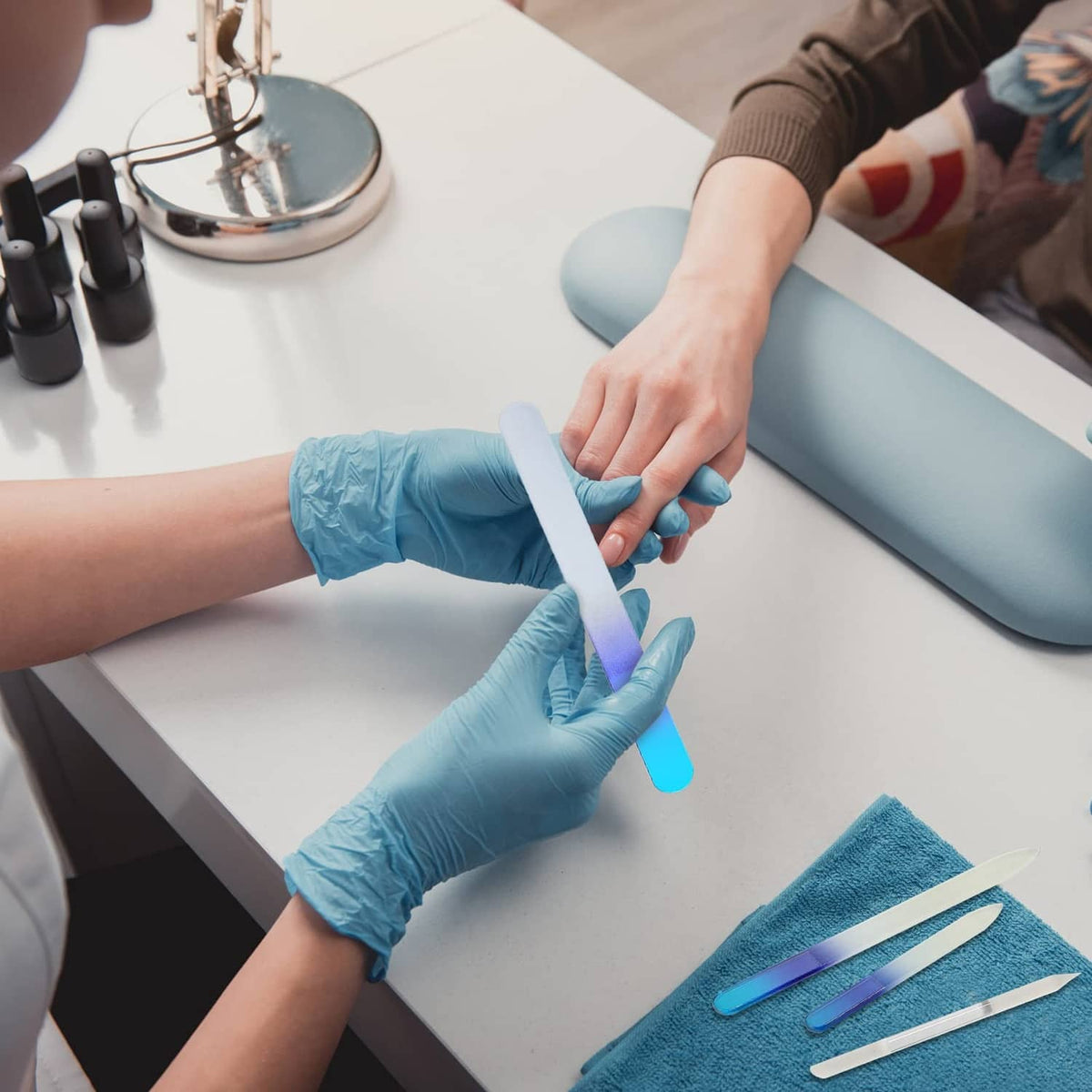 Nail technician filing client nails with a blue-edged glass nail file