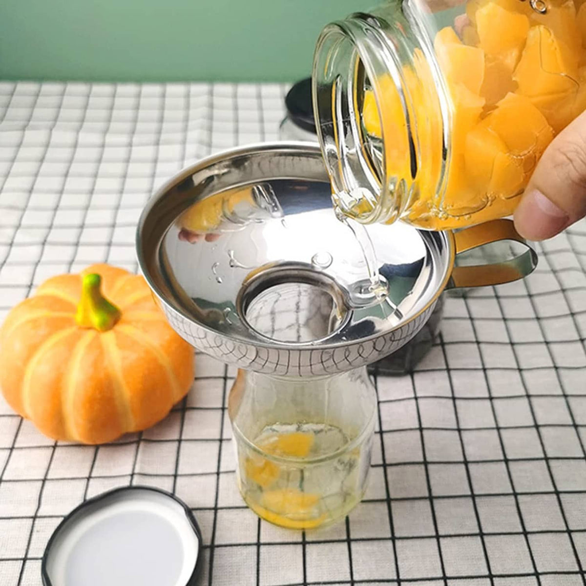 Stainless steel funnel with handle catching liquid from a mason jar during canning