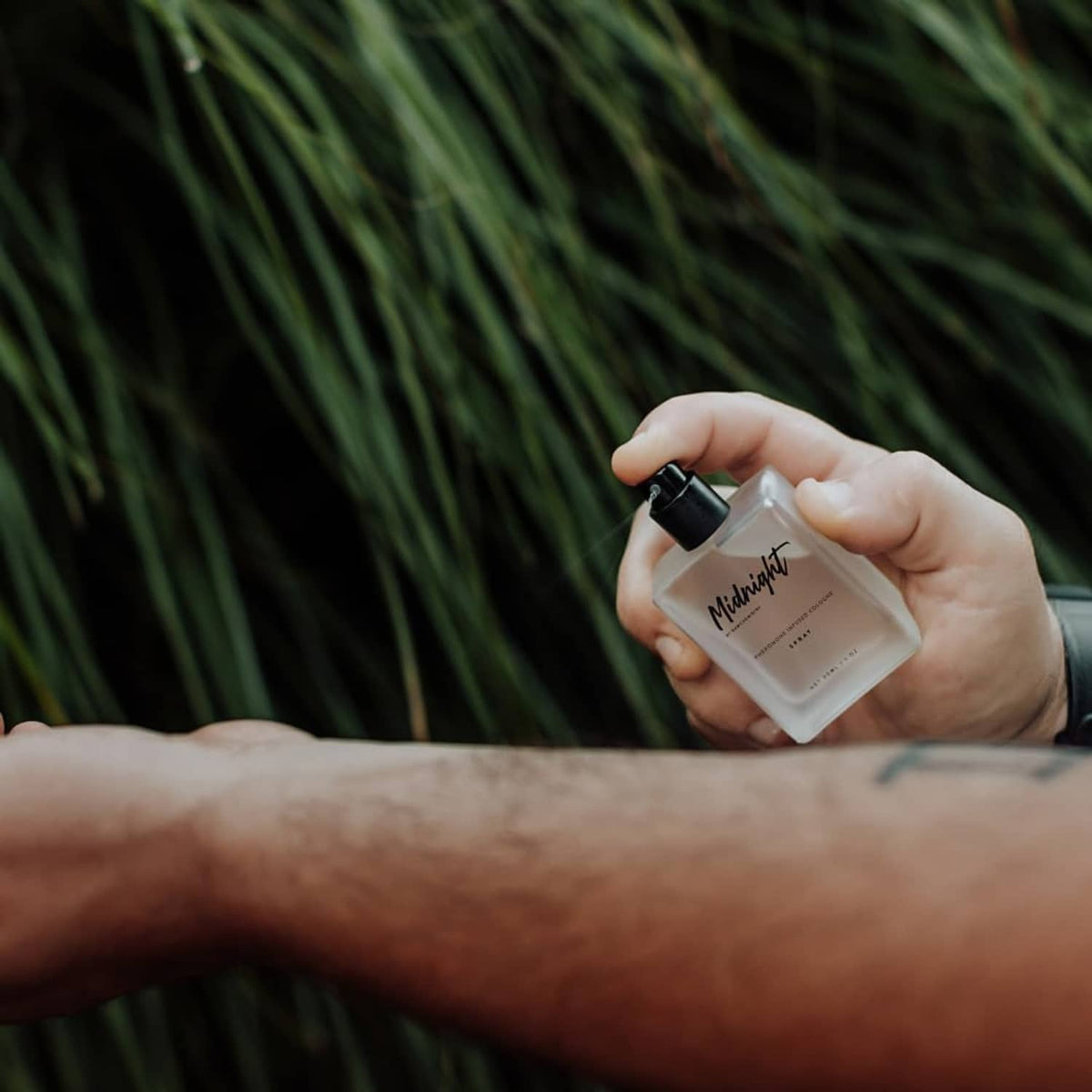 Hand holding cologne spray bottle with black nozzle