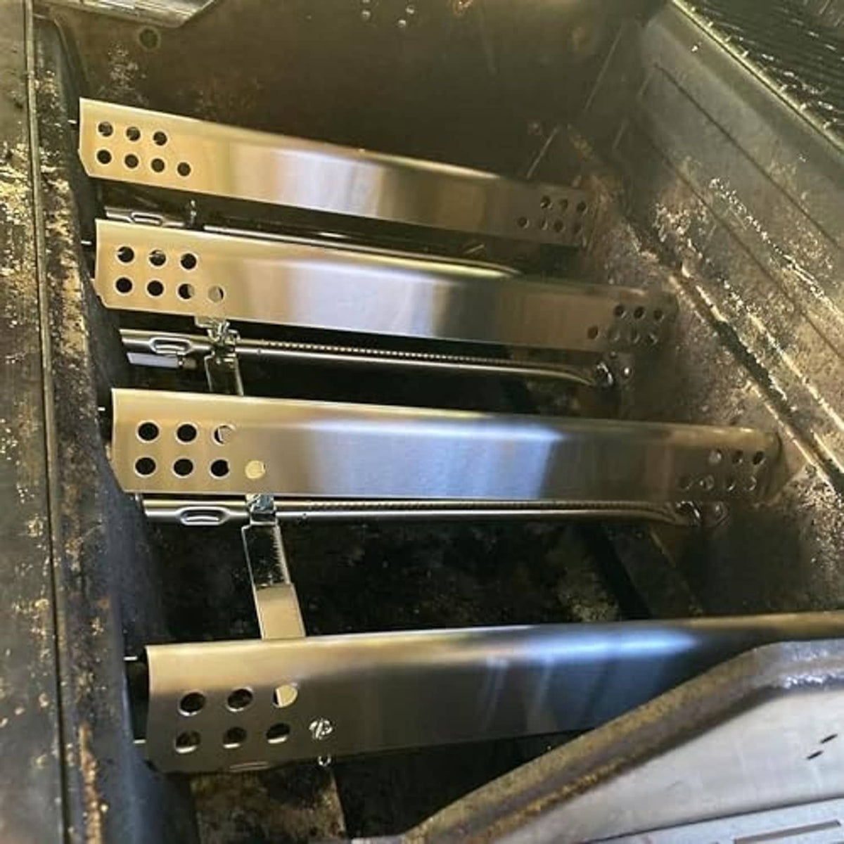 Stainless steel perforated heat plates installed inside a grill firebox.