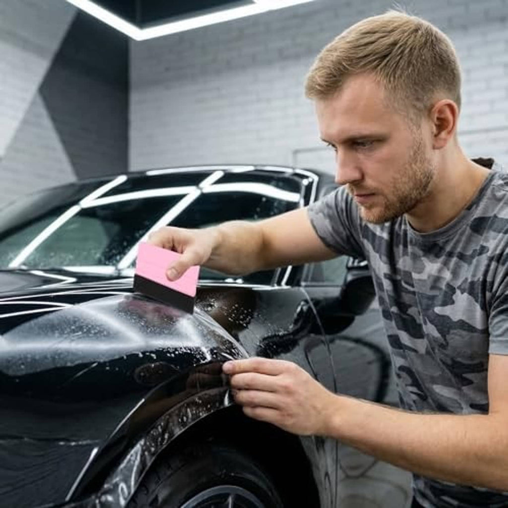 Felt squeegee pressing vinyl film on a car window by a person’s hand