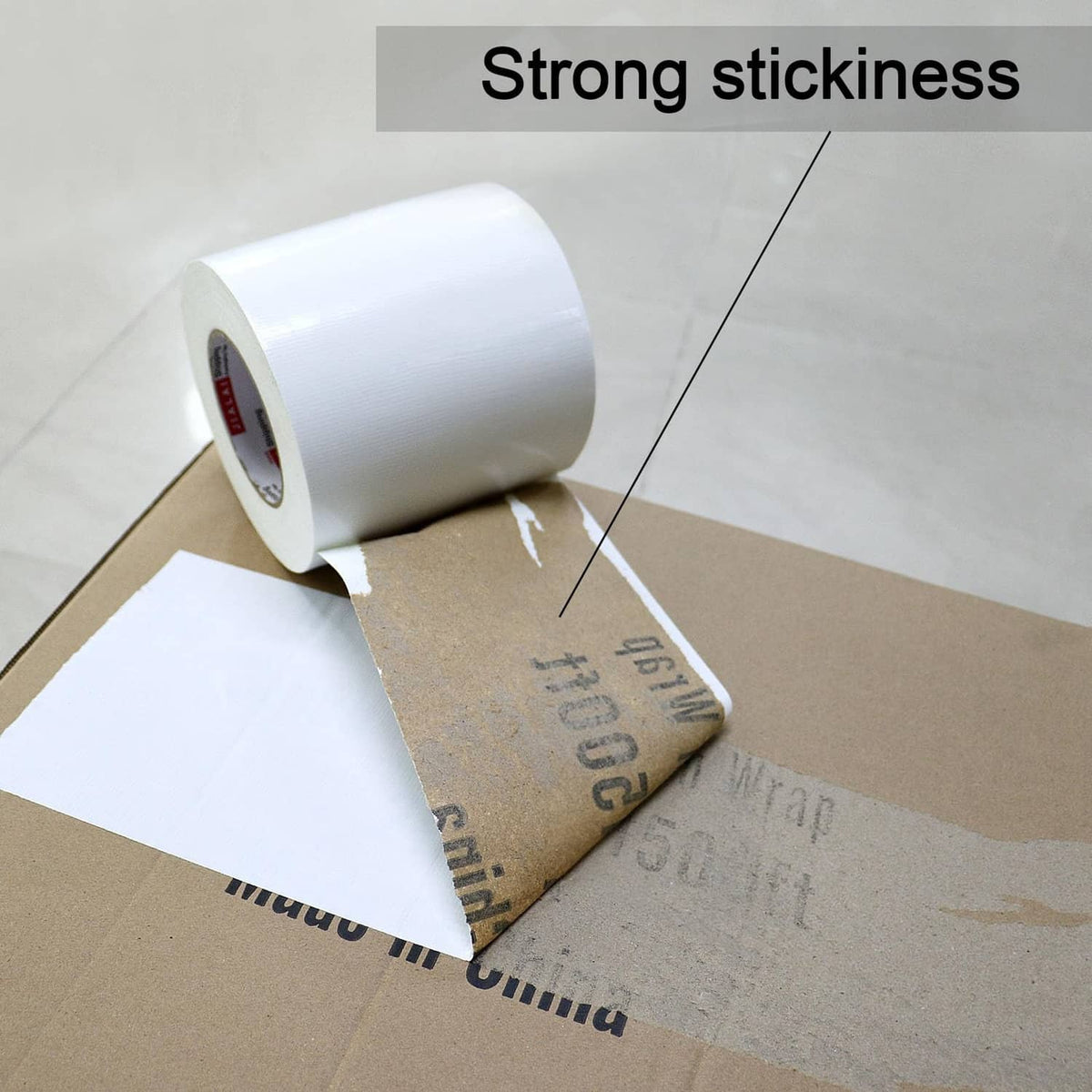 White duct tape roll applying over cardboard and box seam for strong adhesion.