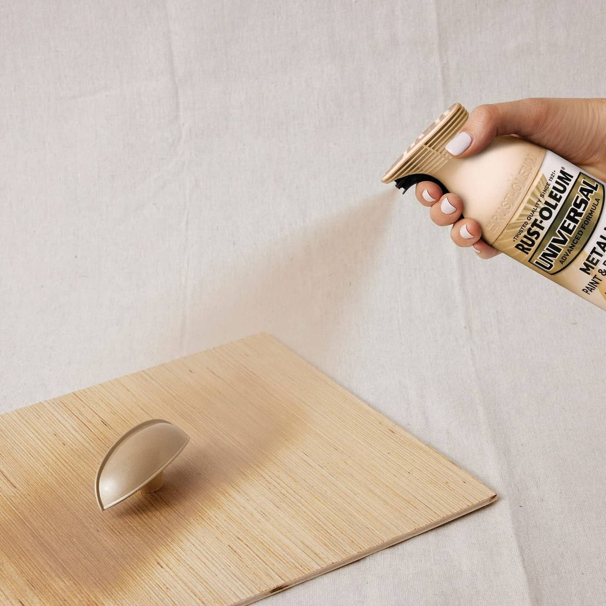 Hand holding metallic spray can, spraying paint onto a wood surface
