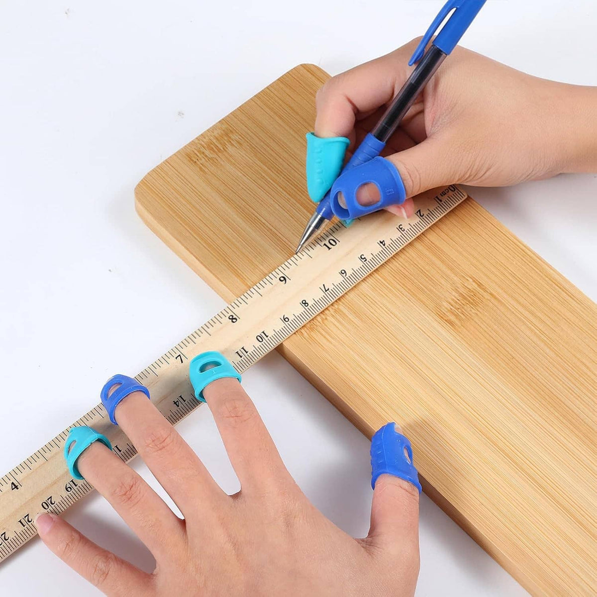 Silicone fingertip protectors on fingers measuring wood with a ruler and pencil