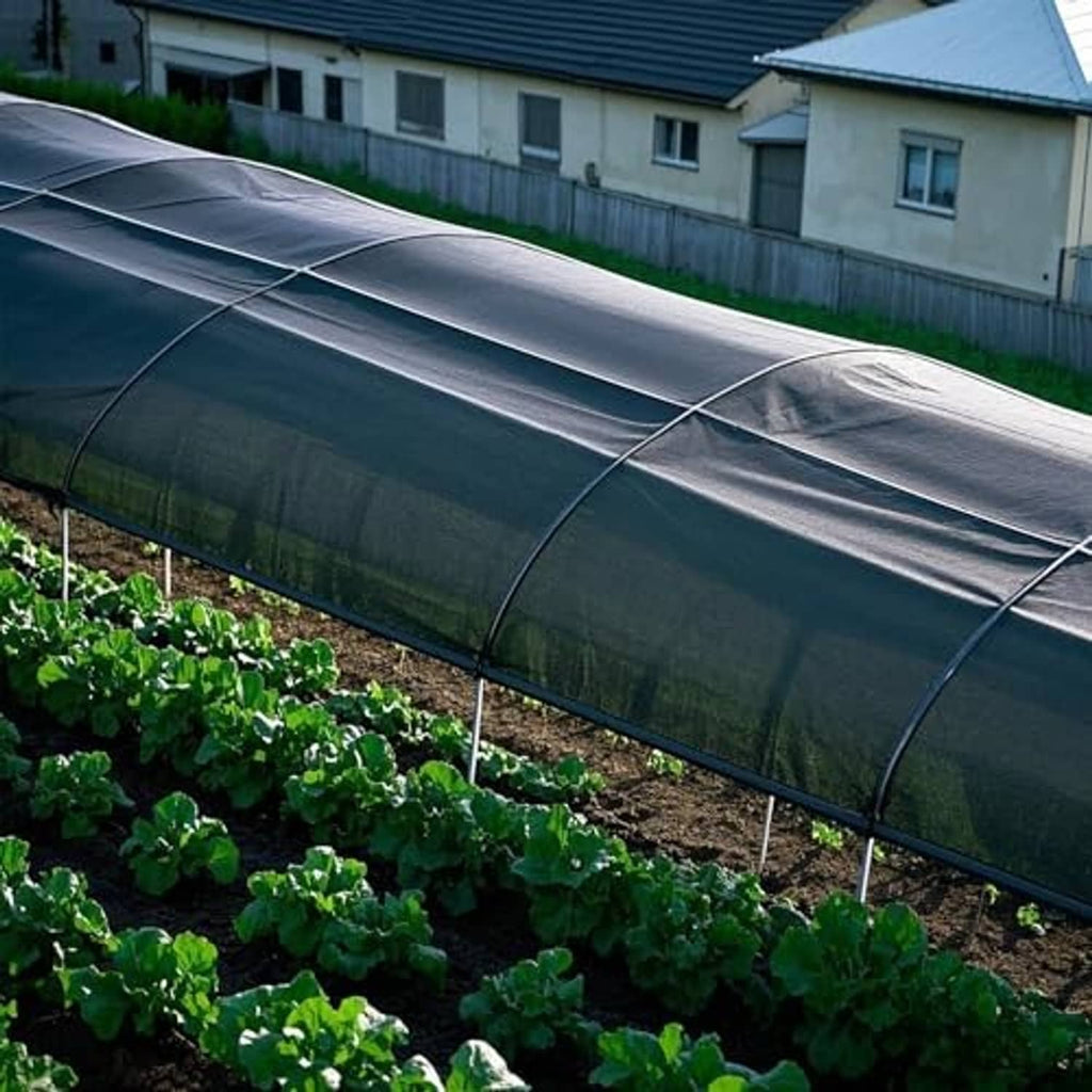 Black shade cloth mesh tarp laid over garden rows on metal supports