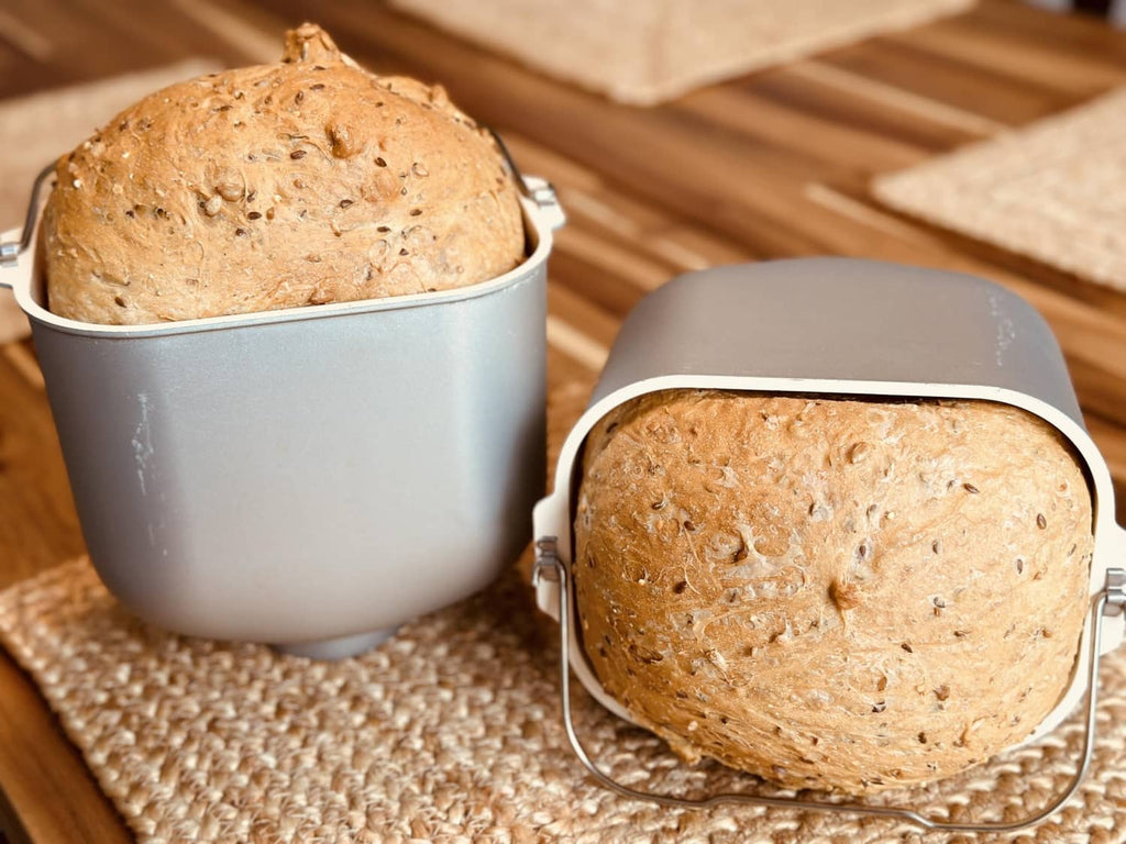 Two baked 8 grain bread pieces in round baking pots on a cloth-lined surface