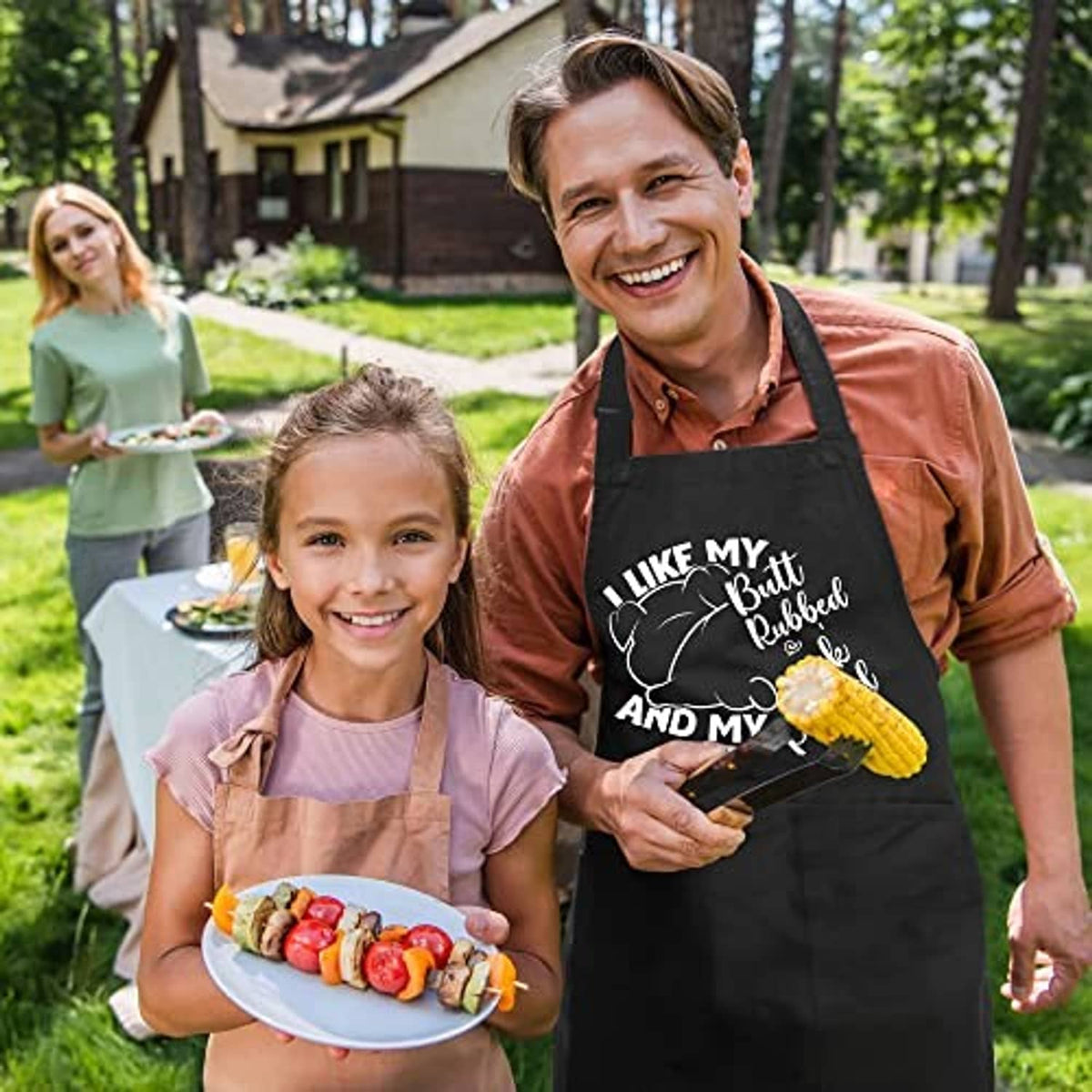 Black grill apron worn by man outdoors, humorous text graphic and utensil icons on chest