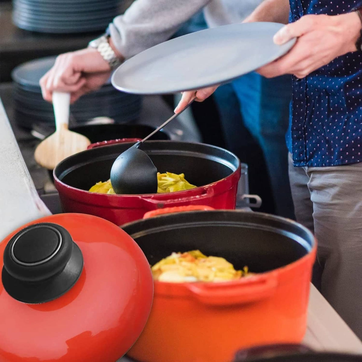Black pot lid knobs on red and black cookware lids on a kitchen counter