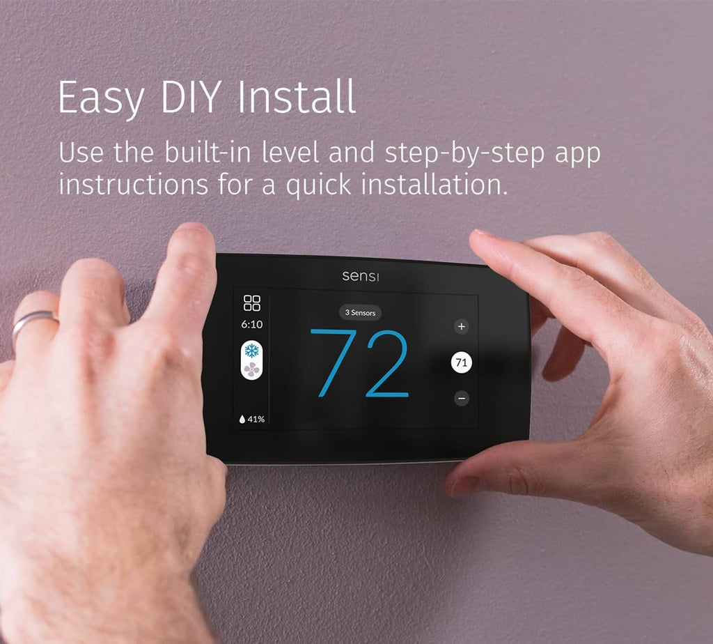 Black touchscreen smart thermostat being installed with hands on the wall