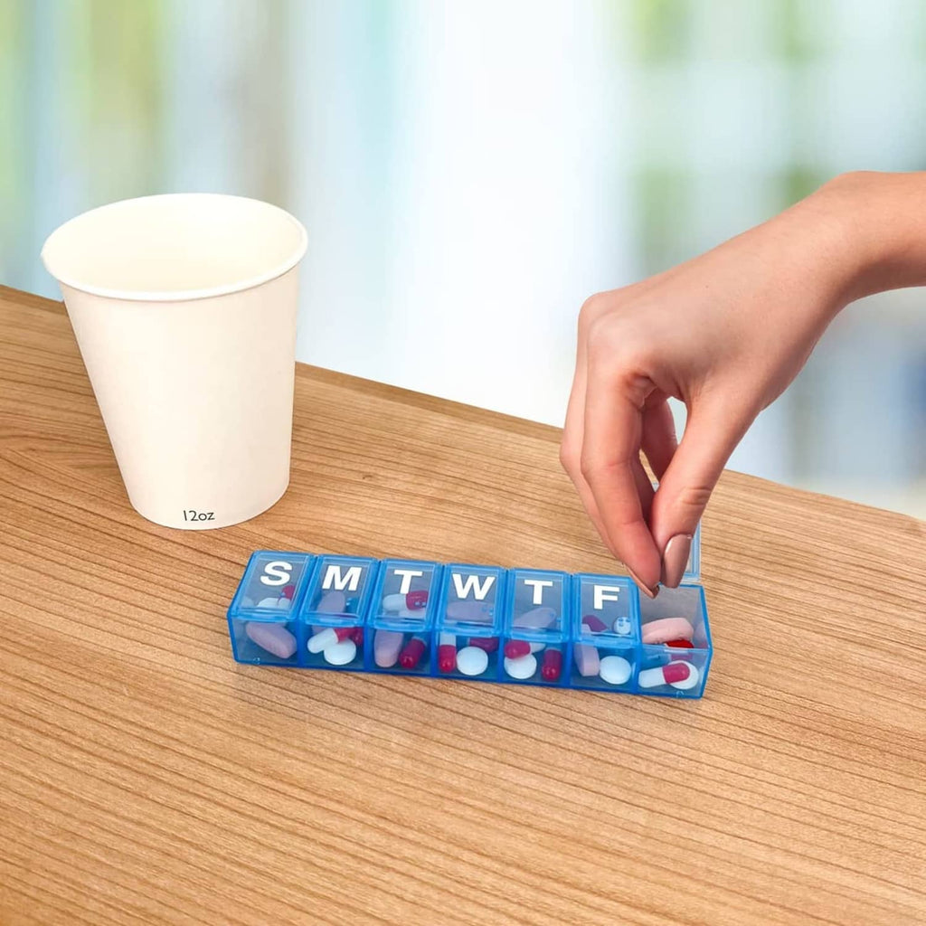 Blue weekly pill organizer with day labels S, M, T, W, T, F on a table