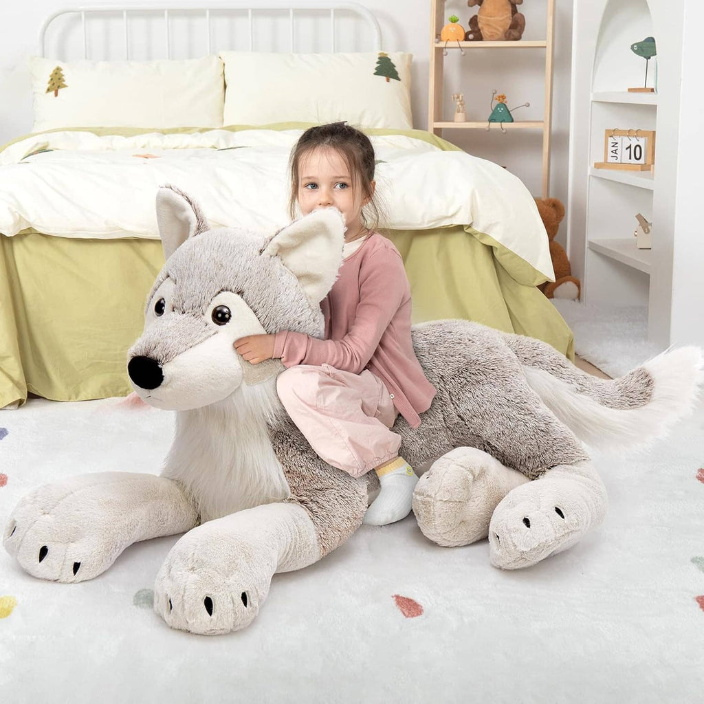 Large gray wolf plush stuffed animal with white muzzle and paws, lying with child