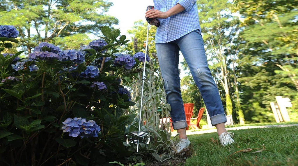 Drill tiller attachment on a lawn near hydrangeas, with metal tines in ground