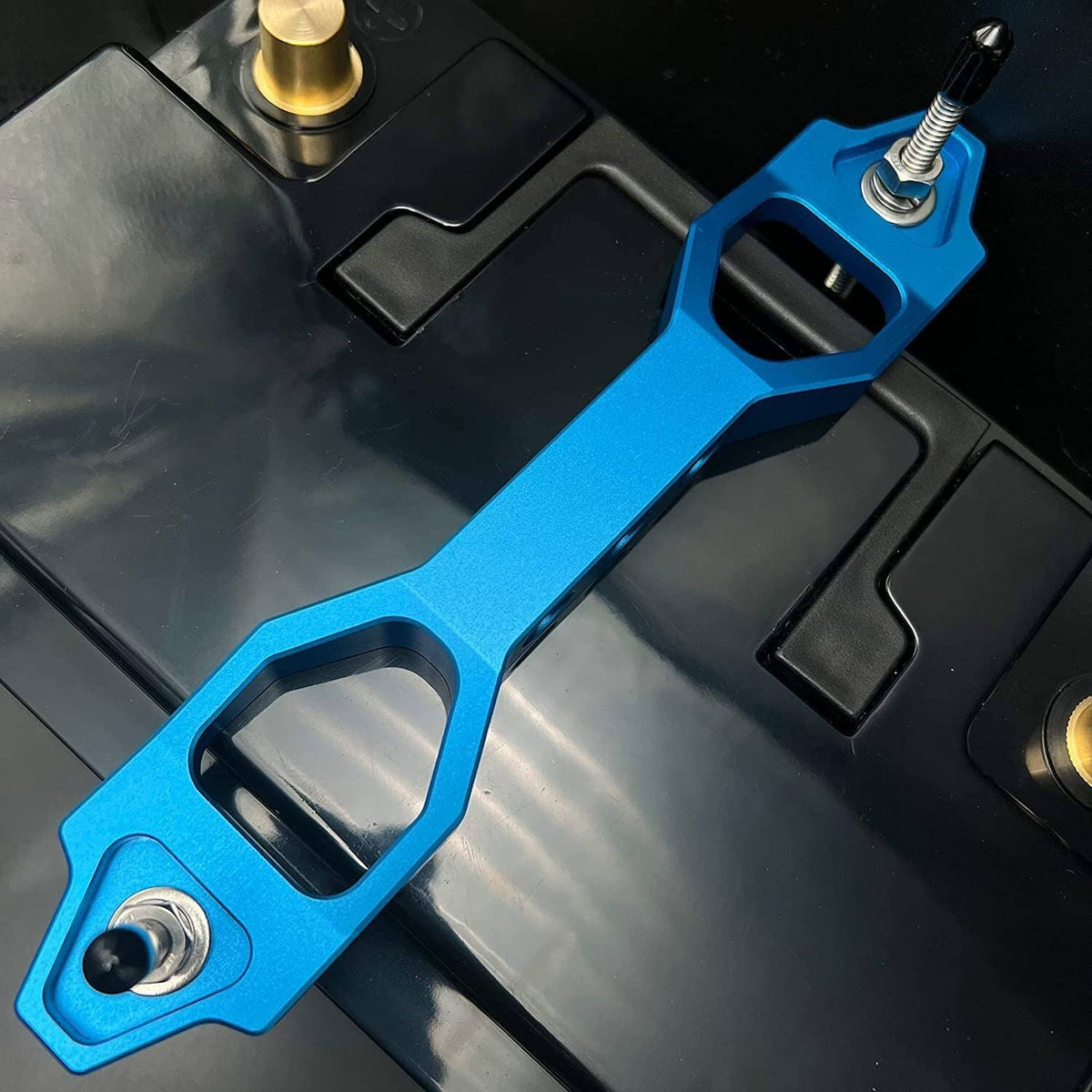 Blue aluminum battery tie-down bracket with threaded stud and bolts on battery case