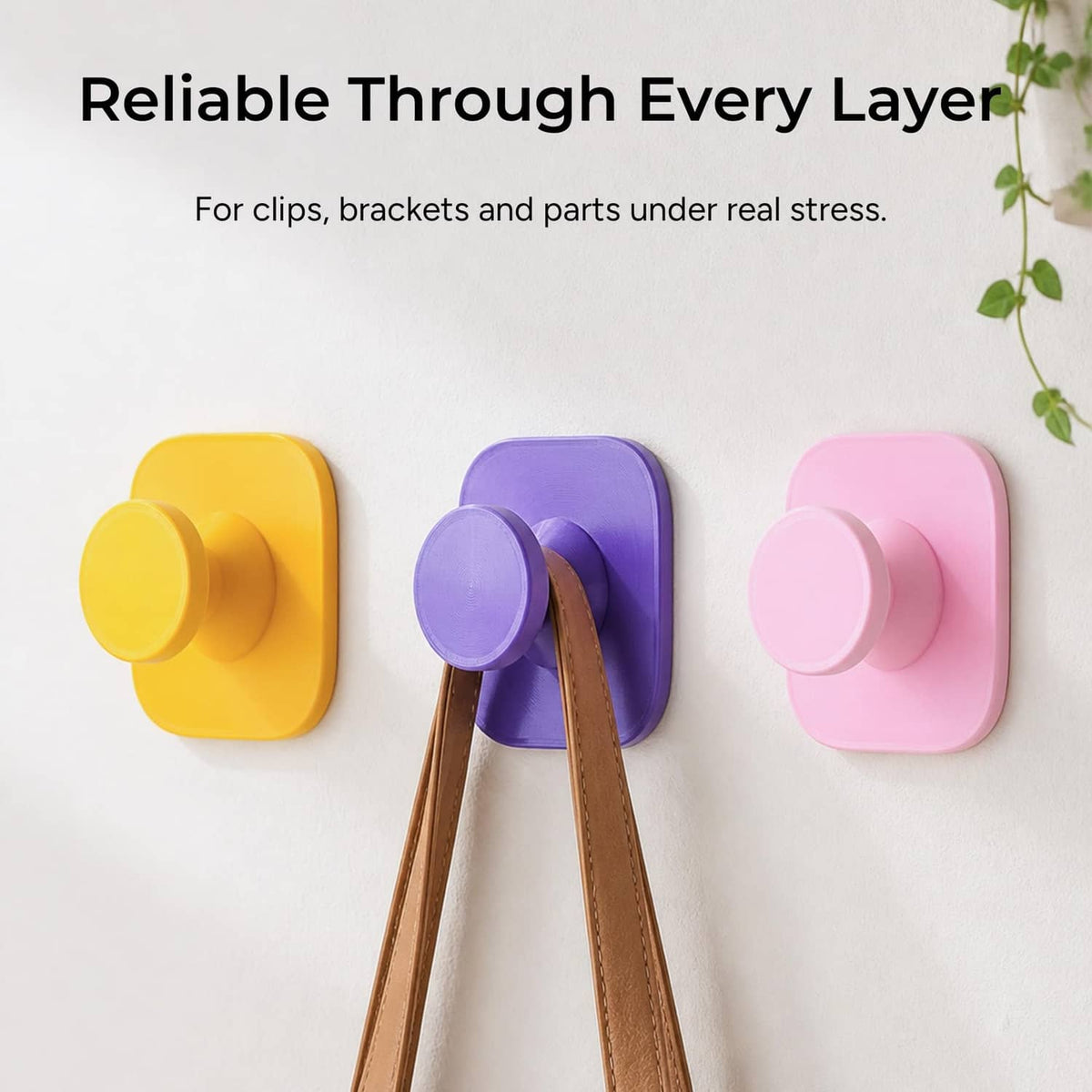 Colorful 3D-printed wall clips: yellow, purple, and pink with central peg