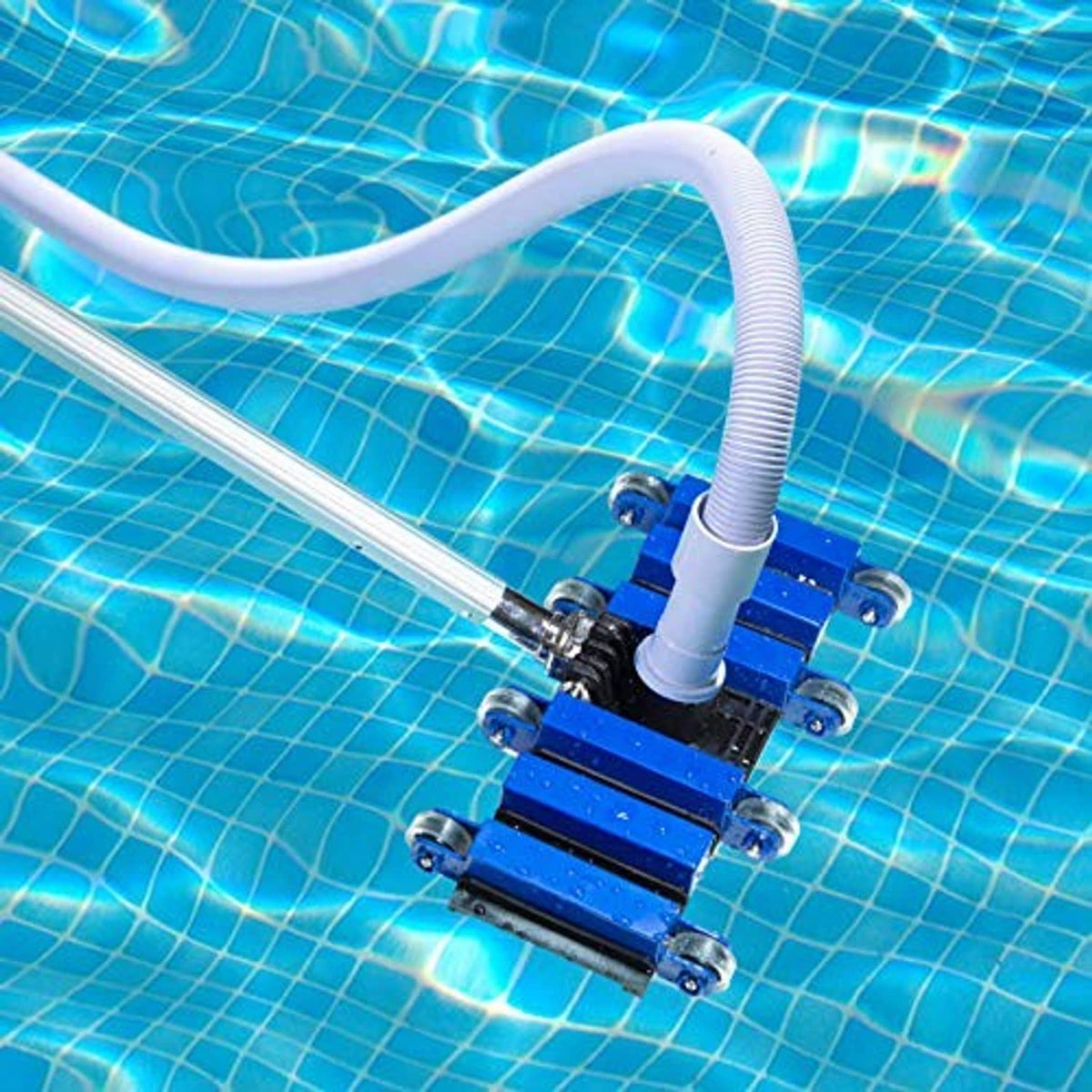 Blue pool vacuum head with wheels and brush plate on pool floor connected to a white hose.