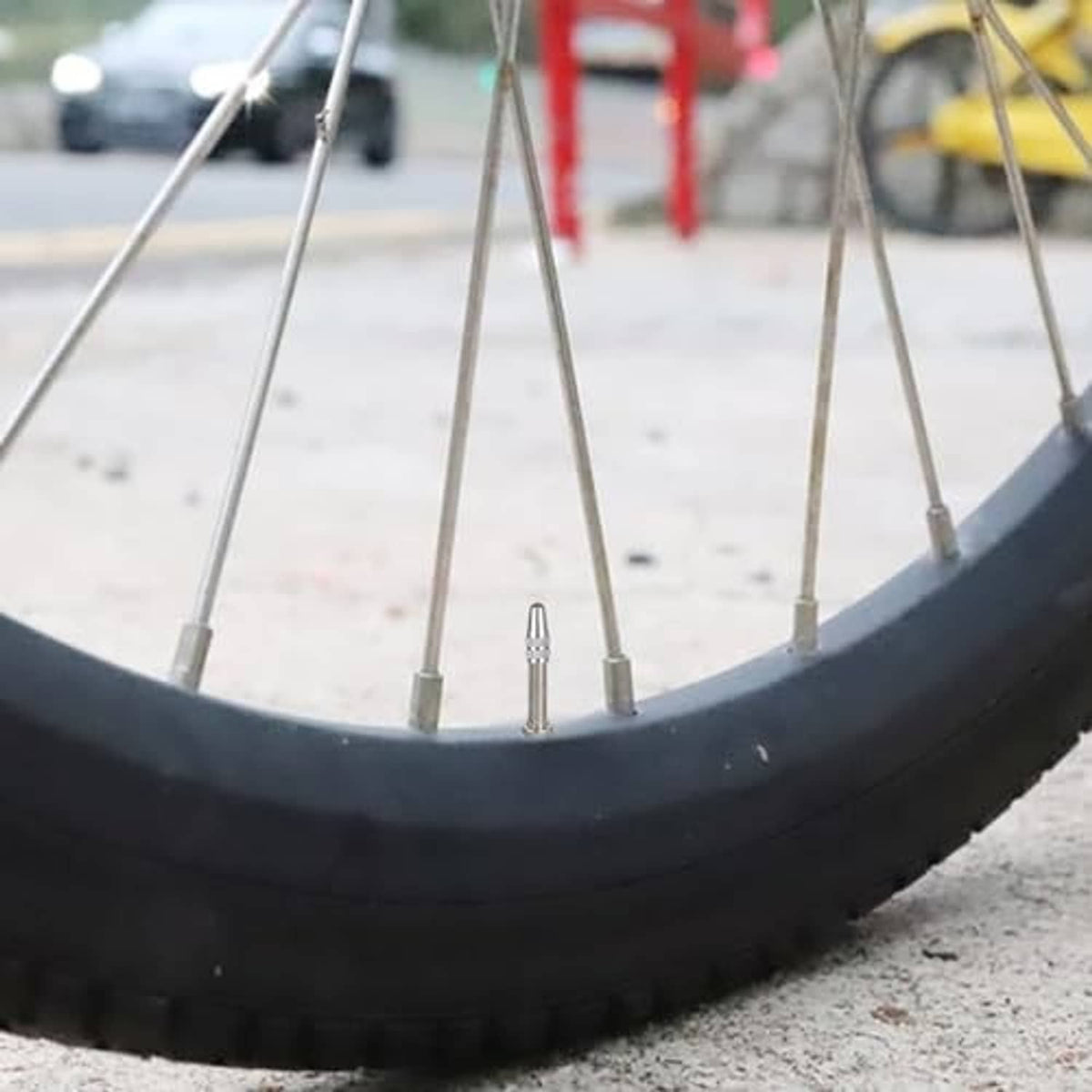 Silver Presta valve cap on a bicycle valve stem, close-up near wheel spokes
